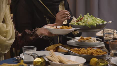 close up of muslim family sitting around table with food for meal celebrating eid being served 1