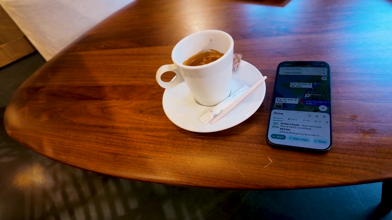 Una toma en picado recorre una mesa de madera con un espresso y una aplicación de navegación en un smartphone.