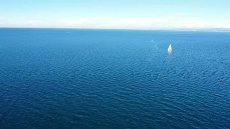 aerial push from shore to sea with sailboat in background on blue sea