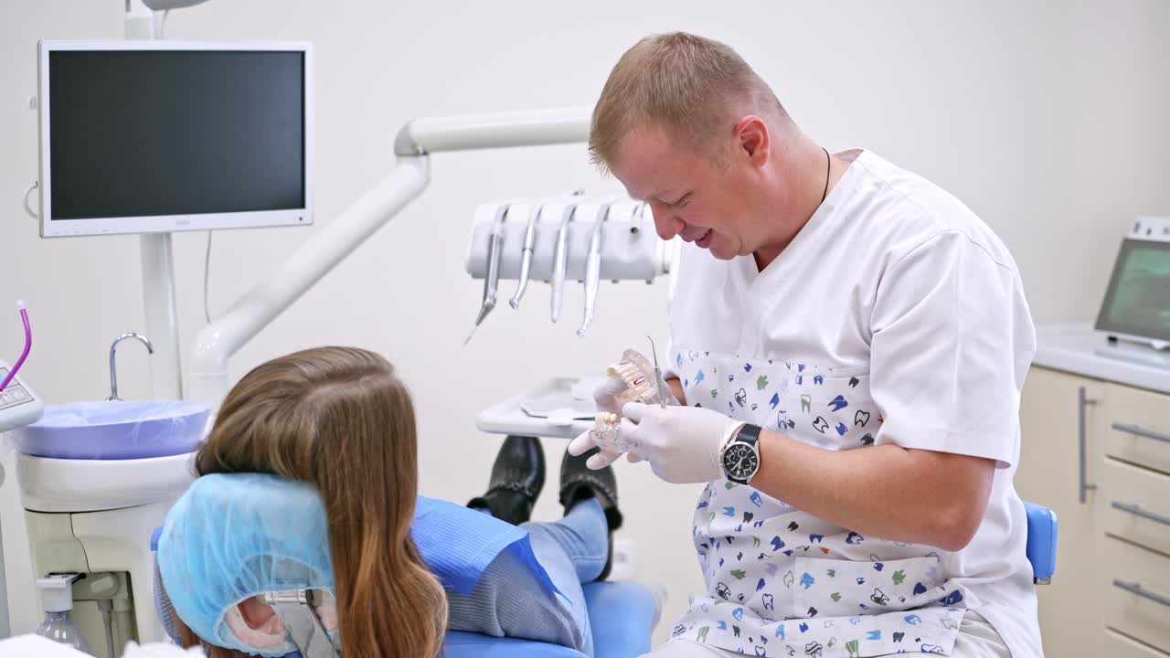 Stomatologist with jaw model and a patient in clinic. Dentist talks to a female patient using artificial teeth in modern cabinet. Dental treatment, medical concept.