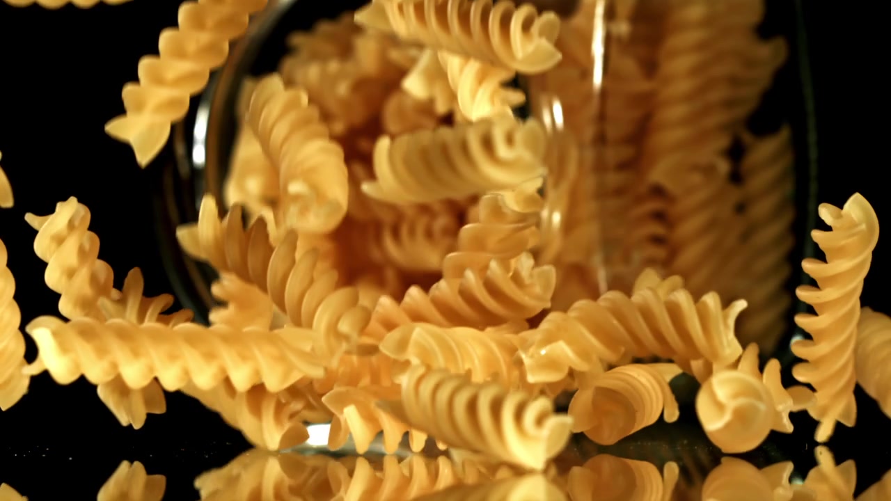 Pasta fusilli cruda che cade da un barattolo di vetro al rallentatore