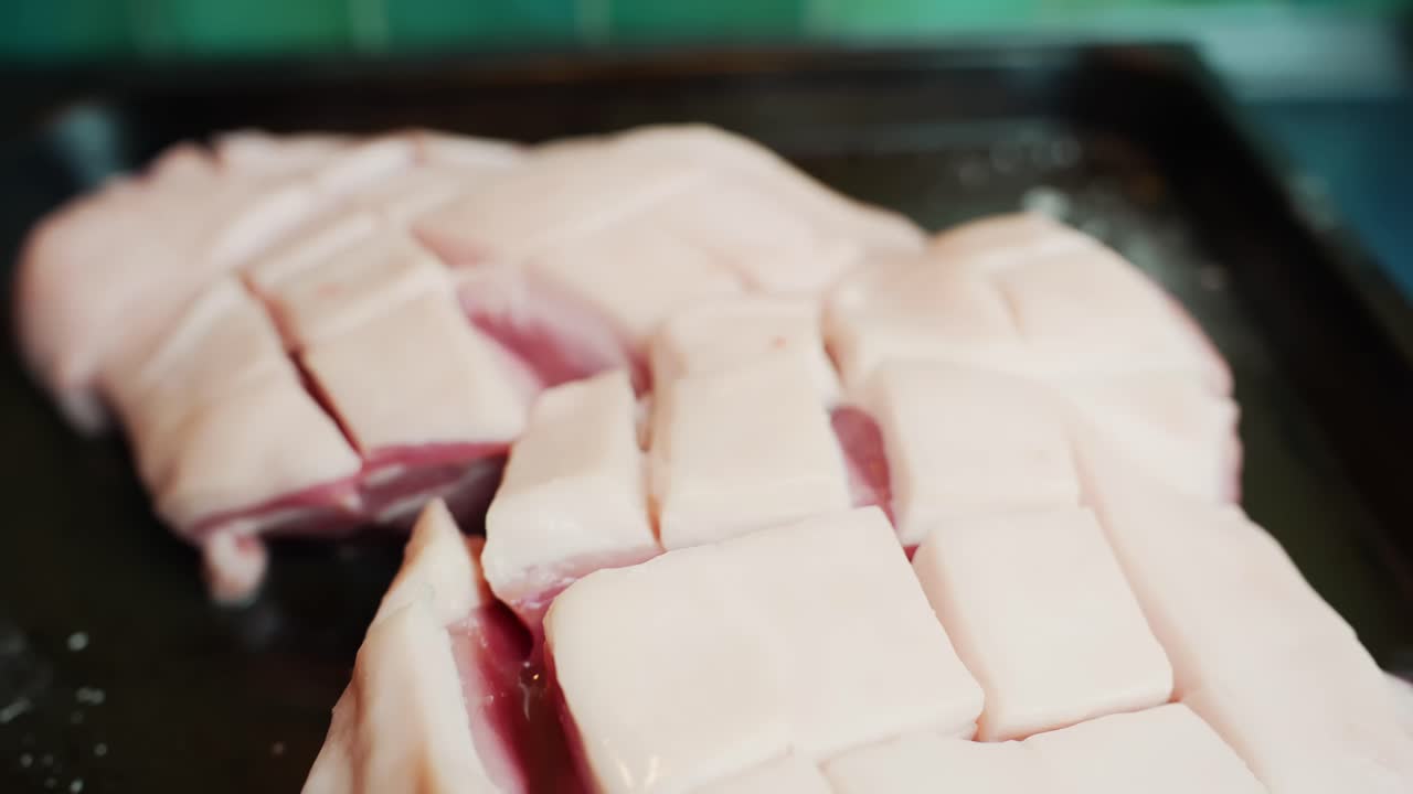 Close-up of scored pork belly on a roasting tray with salt crystals, ready for baking. Shallow depth of field food prep on a kitchen counter