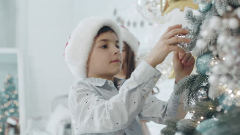 Serious-boy-decorating-christmas-tree-in-living-room.