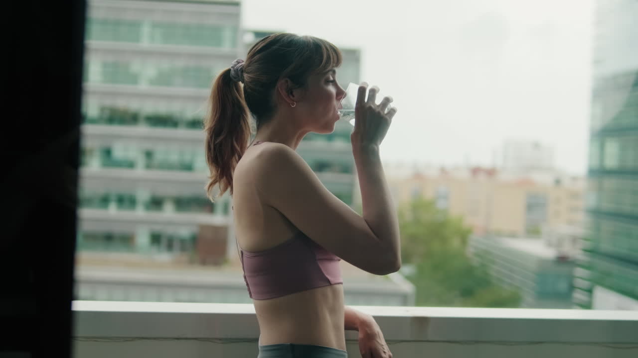 Woman Hydrates on Balcony After Fitness Workout