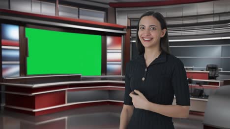 Happy-Indian-female-news-anchor-pointing-at-green-screen-and-showing-okay-sign