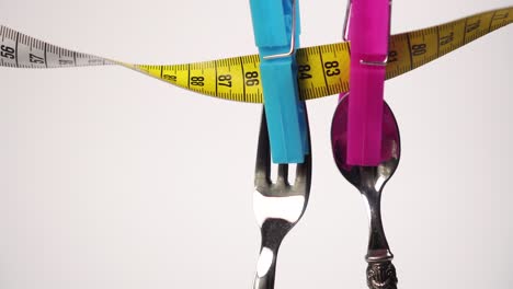 spoon and fork are dried on a yellow white centimeter, fixed with pink and blue clothespins on a white background.