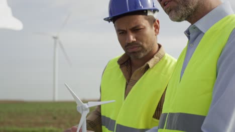 team of caucasian and latin engineers standing on wind turbine field and discussing over project.