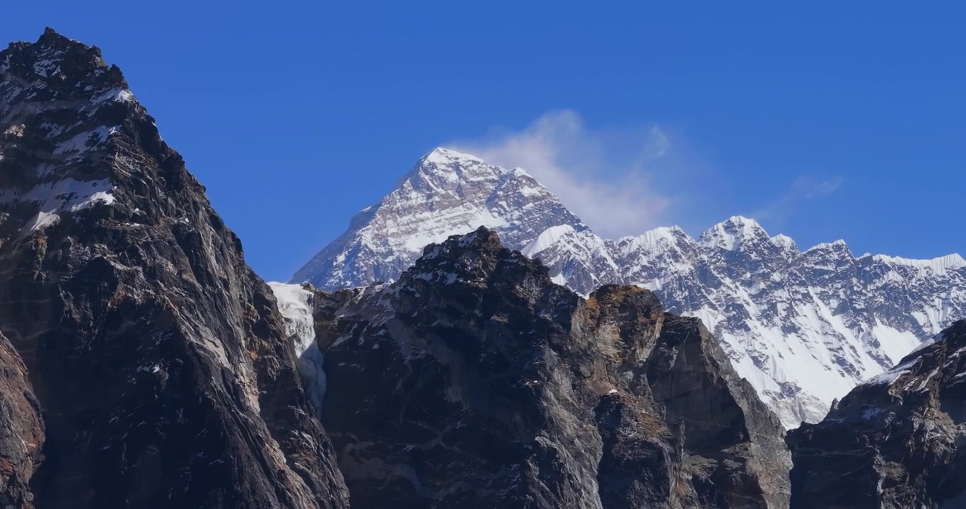 Everest-regionen, Nepal, drone luftfoto sidelæns glidende skud, der bevæger sig forbi mørke, barske klippefyldte bjergrygge i forgrunden for at afsløre den sneklædte top af Mount Everest i baggrunden