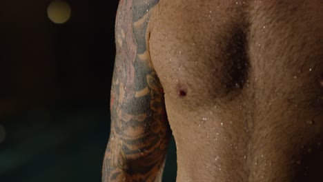 hombre con tatuajes junto a una piscina por la noche