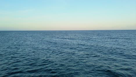 soft sunset light glows on horizon as drone flies above open ocean deep blue water