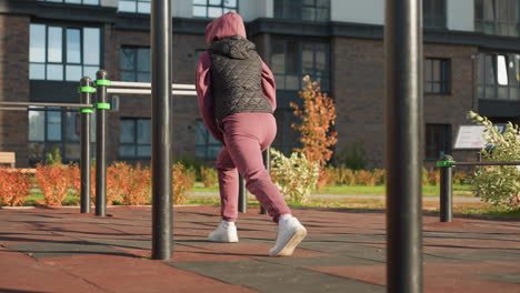 back view of active woman in sports wear doing split squats with hands placed on legs in urban park setting with modern railing flowers shadows on tile ground under bright sunlight