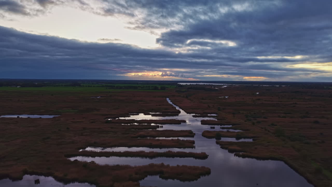 Omfattende vådområde i skumringen med rolige vande, der afspejler den farverige himmel og silhuetter af fjerne træer
