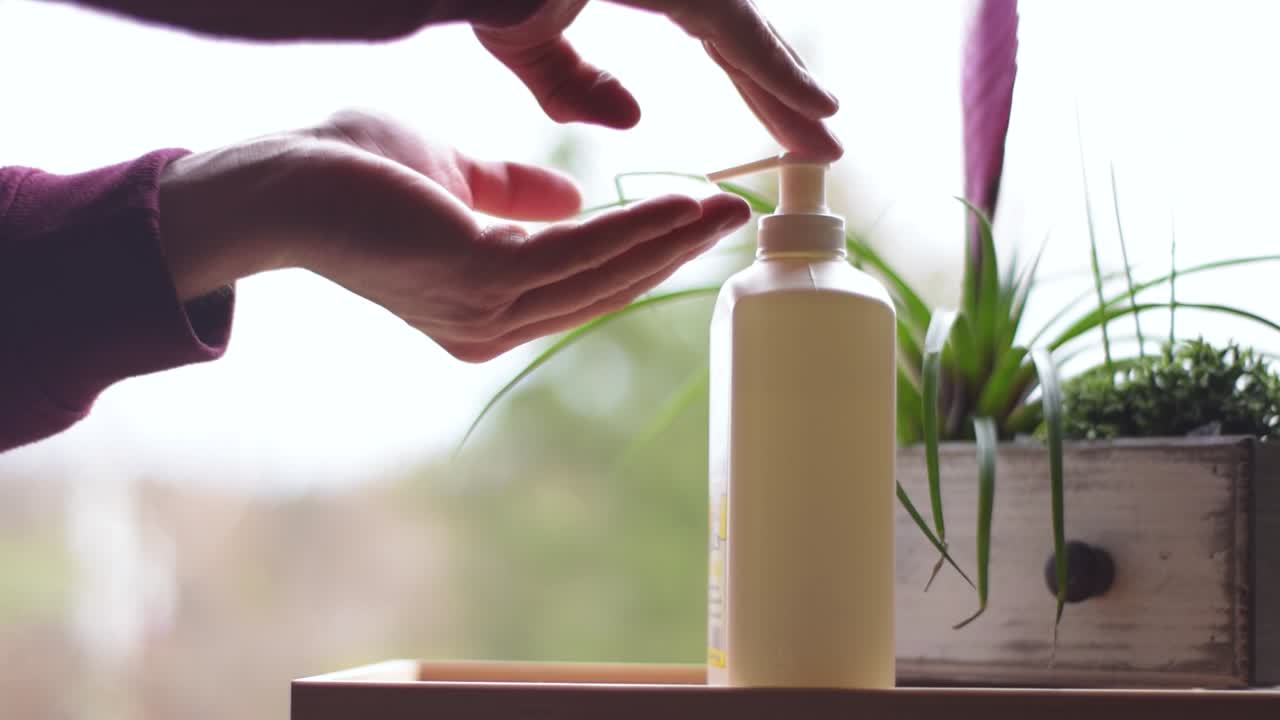 Two male hands getting dose of hand sanitizer gel out of a dispenser.