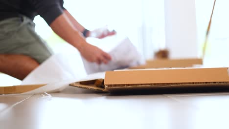 a person unpacks a box on a table in a sunlit room, focusing on careful handling and organization
