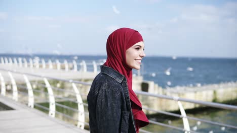 attractive muslim girl with hijab is smiling and going back and forth, enjoying her sea side walk. free time activities. outdoors footage