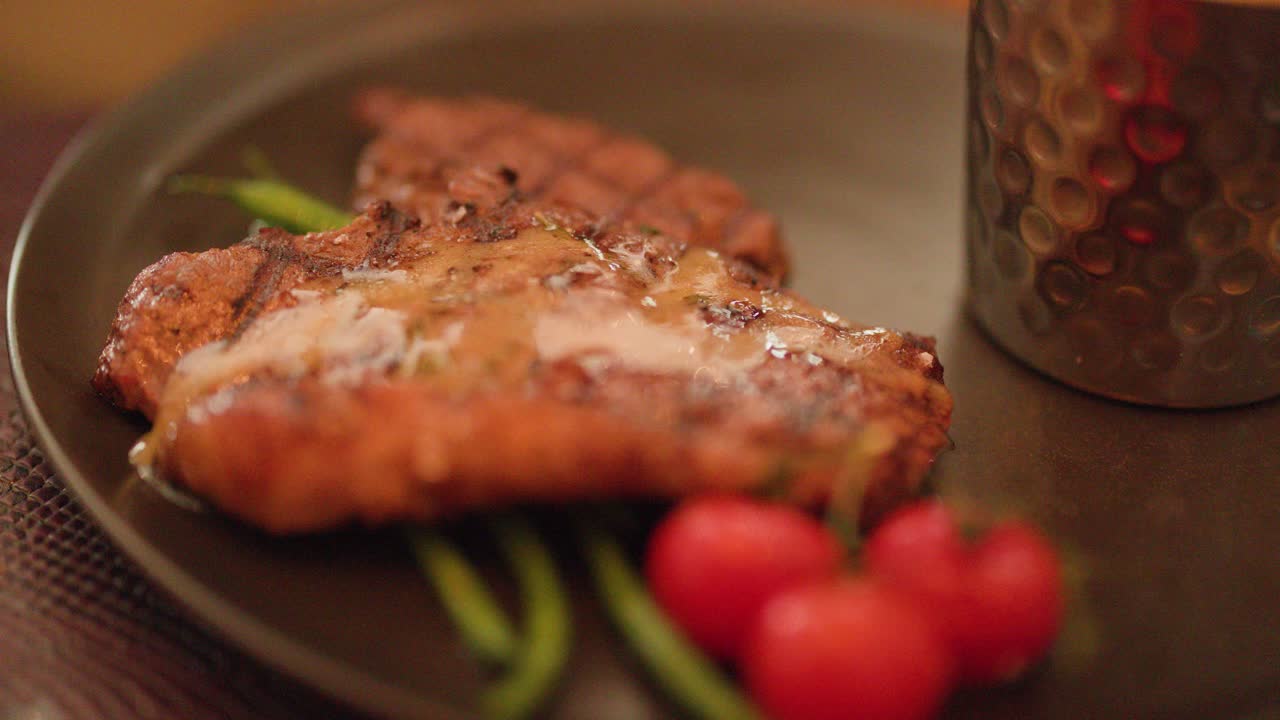 Juicy grilled steak with melting butter, asparagus, and tomatoes under warm, soft restaurant lighting