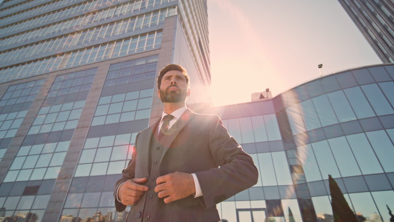 un hombre de negocios presentable ajustando su traje en una calle soleada cerca de un rascacielos moderno.