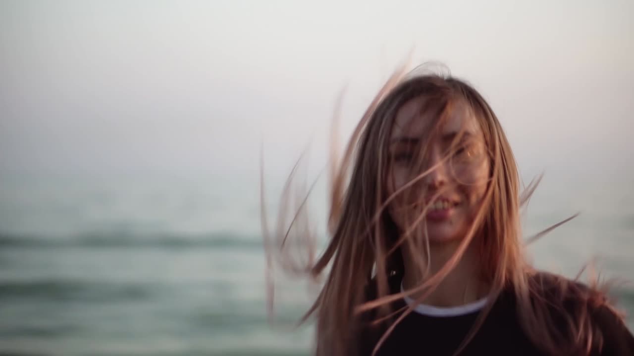 긴 머리카락의 여자가 가을 해변을 따라 행복하게 달리고, 카메라를 보고 있습니다.