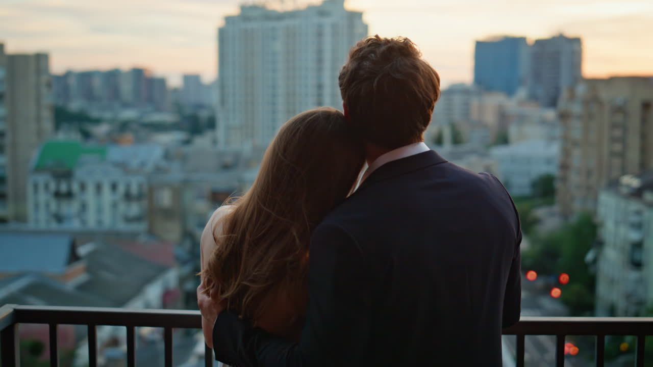Affectionate boyfriend hugging girlfriend on balcony gazing evening city closeup
