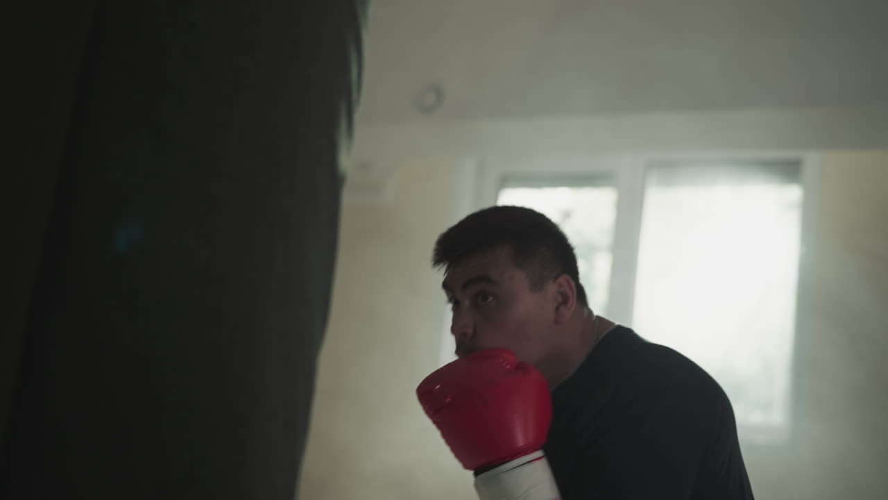 Fighter exercises with punching bag blocking face in gym. Professional sportsman beats equipment against window in boxing club slow motion. Combat arts show