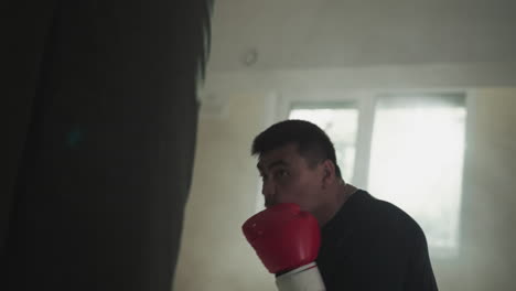 fighter exercises with punching bag blocking face in gym. professional sportsman beats equipment against window in boxing club slow motion. combat arts show