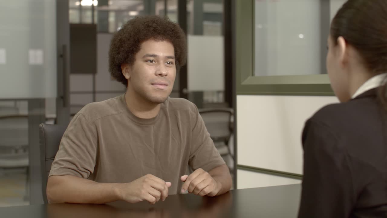African American male in his 20's with a woman talking in an office setting with dolly video shot moving left to right