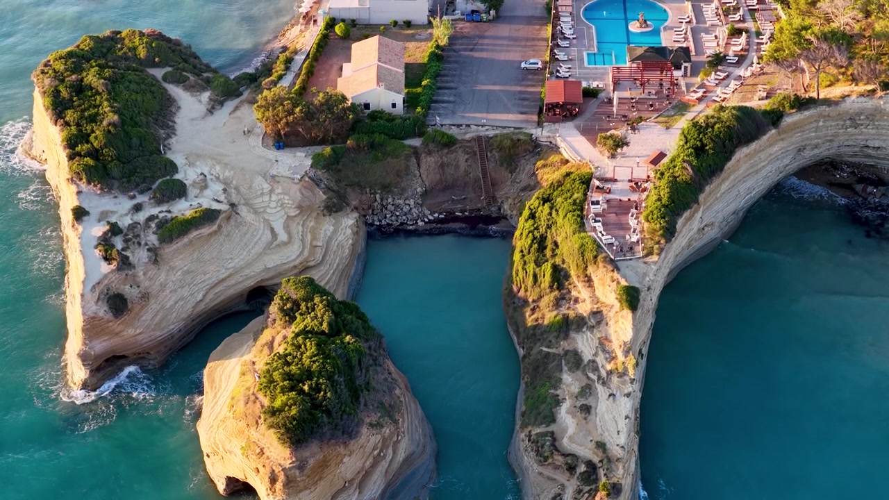 Vue aérienne du Canal D'Amour à Sidari, Corfou, Grèce. Prise de vue par drone en tilt-up révélant des formations rocheuses uniques en grès, de l'eau de mer turquoise, des falaises côtières et un complexe hôtelier de luxe avec piscine.