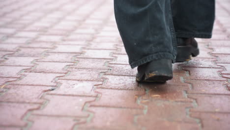 back shot of person's legs running during light snowfall wearing black jeans and black boots, autumn leaves scattered across path, creating peaceful winter atmosphere with light breeze