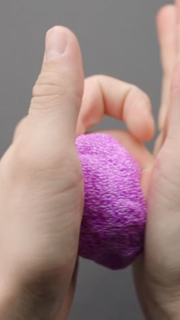 vertical. hands pressing and squeezing a textured pink foam slime against a neutral gray background, showing bead details