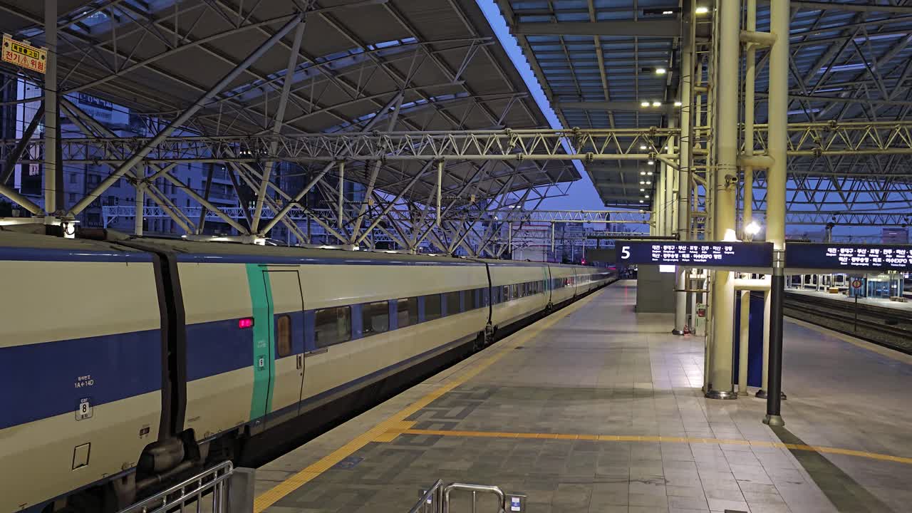 Descending along escalator to empty concrete platform at dusk with KTX train waiting, doors closed with no people around