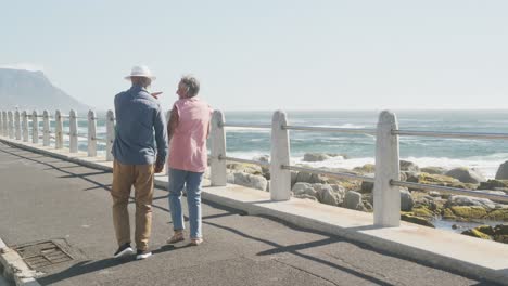 Happy-senior-african-american-couple-walking-along-promenade-by-the-sea,-slow-motion