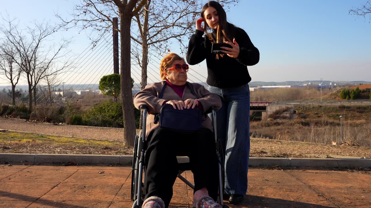 Granddaughter and grandmother in a wheelchair taking a selfie in a park
