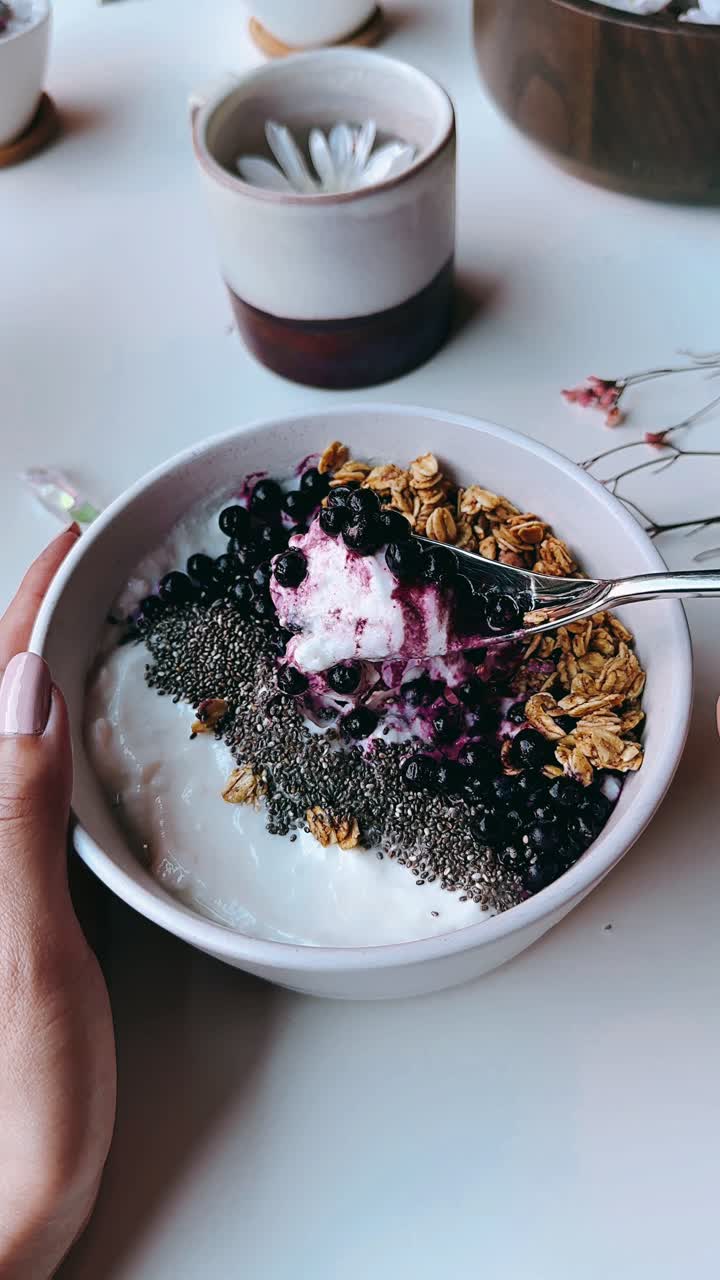 Mano che regge una ciotola di yogurt con granola, mirtilli e semi di chia