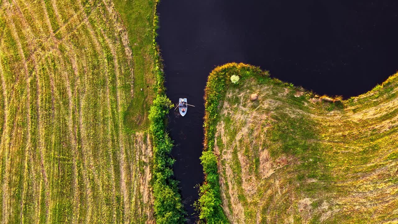 Aerial top view of a man rowing boat using oars on river with grassy banks either side