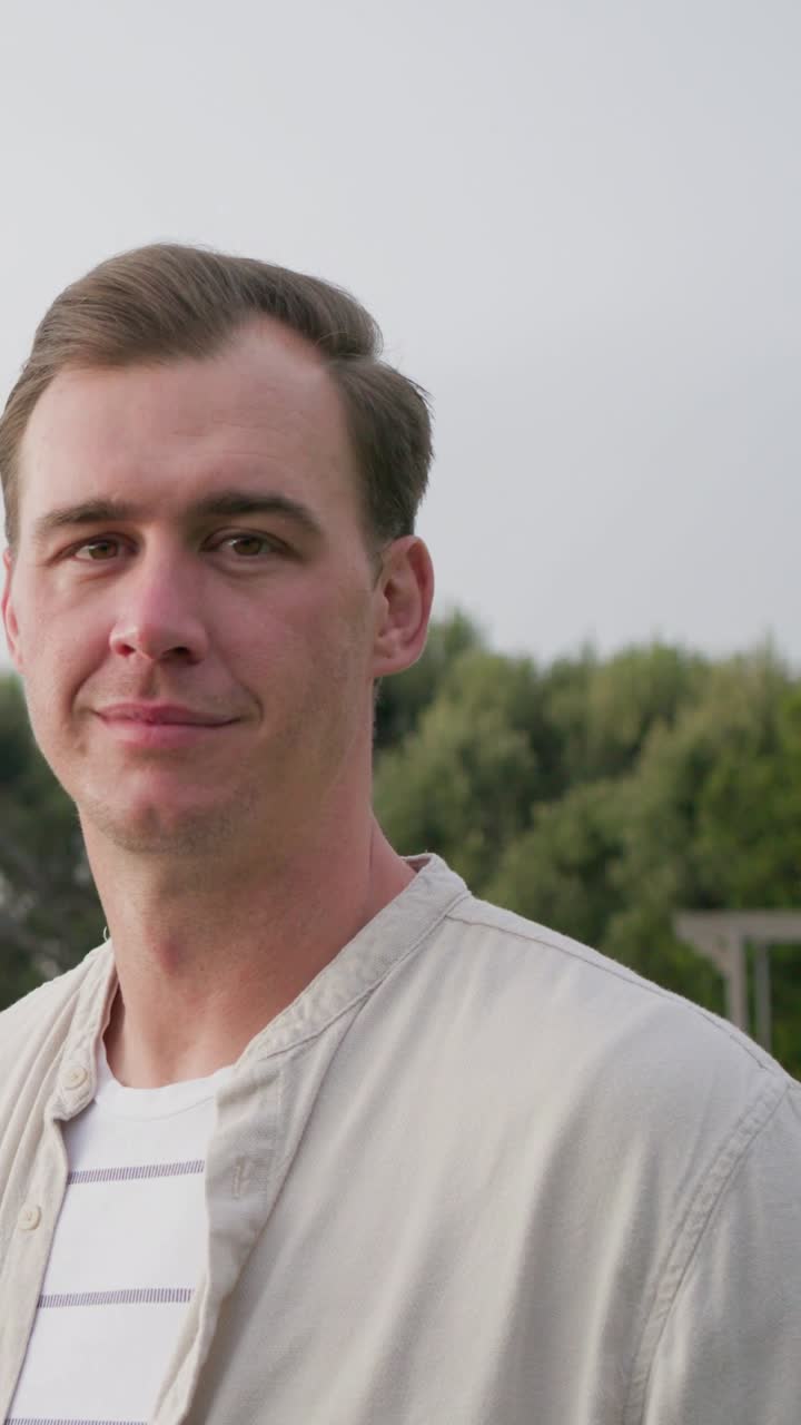 Vertikal video: Mann snur seg mot kamera, smiler ved trekanten i beige jakke og stripete t-skjorte