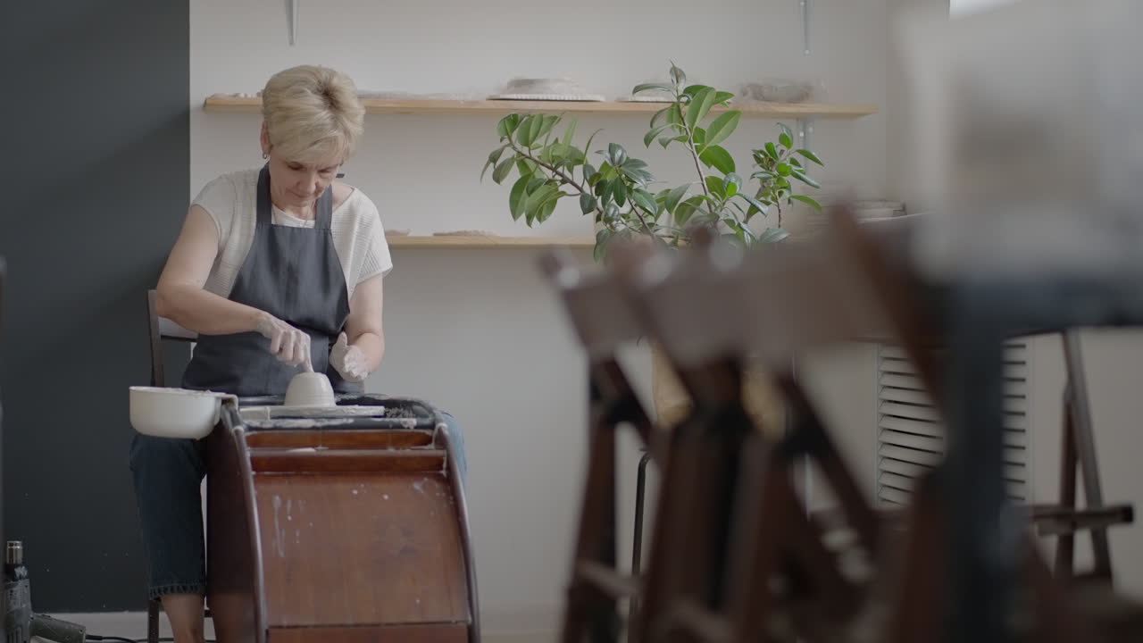 Elderly woman craftsman working on a potter's wheel for making clay and ceramic jugs and plates in slow motion