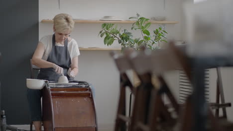 elderly woman craftsman working on a potter's wheel for making clay and ceramic jugs and plates in slow motion