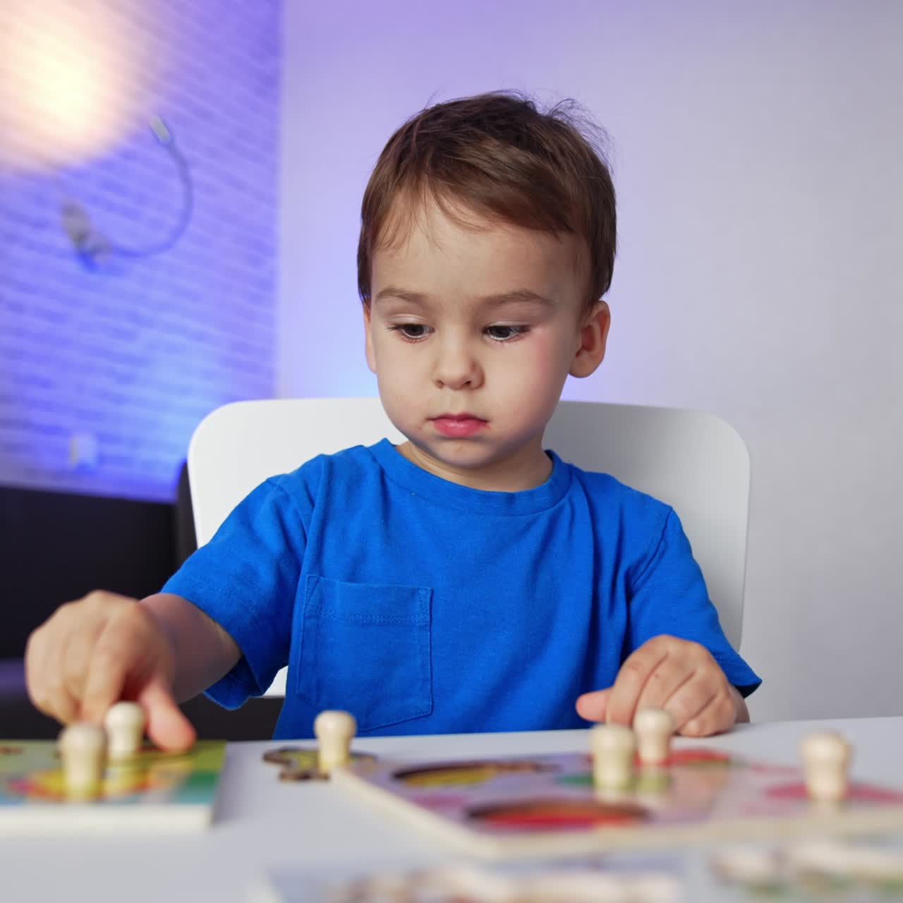 Adorabile bambino moro con una maglietta blu seduto alla scrivania. Un bimbo di due anni che compone puzzle tranquillamente