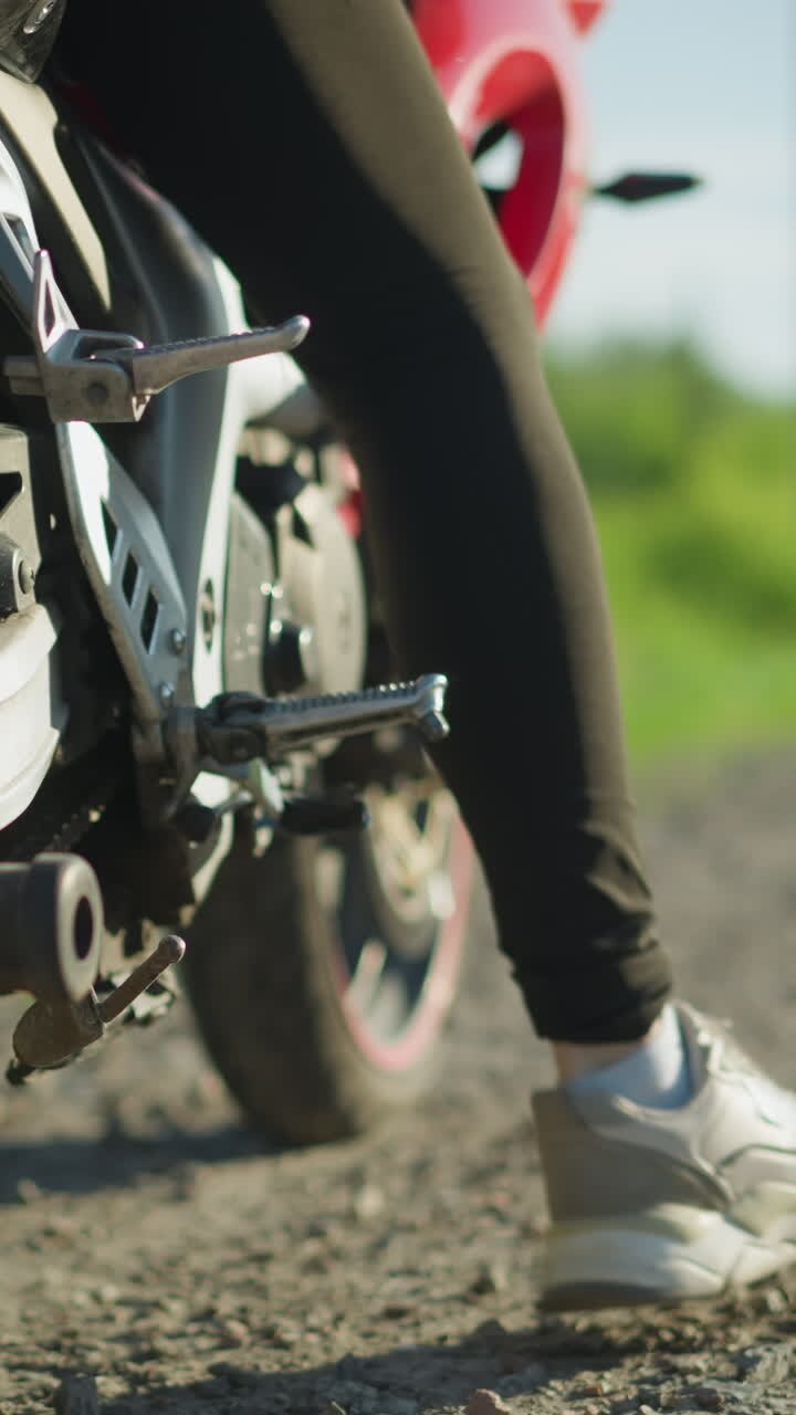 Close-up of a biker adjusting the kickstand of a motorbike, with a blurred background showing a car approaching from a distance