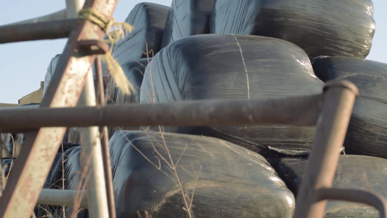 Silage bag storage in farmers field through view of gate tilting crane shot