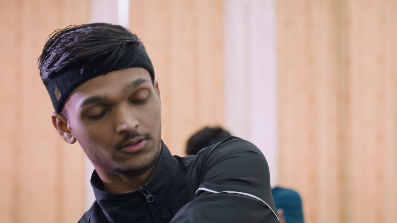 Close up of two athletes wearing headbands engaged in exercise session indoors, stretching arms with intensity and focus during warmup routine before sports activity in training hall