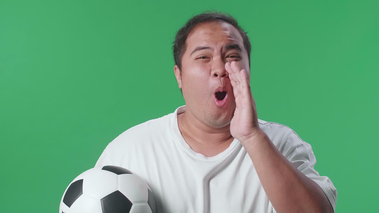 primer plano de un hombre asiático con una pelota burlándose de los perdedores por ooh cara mientras aplaude el fútbol en el fondo de la pantalla verde