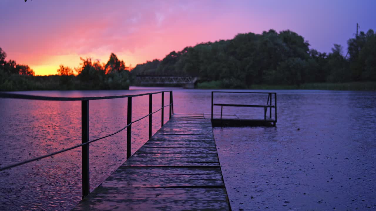 Empty wooden bridge over the river during the rain at sunset. The footbridge in the lake on the background of trees in the evening.