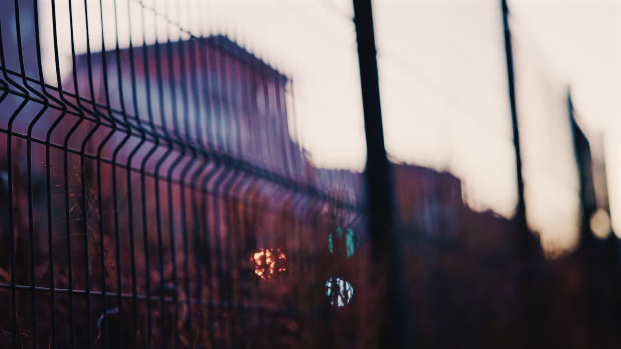Close up of a metal fence with softly blurred lights of a train passing in the background at dusk