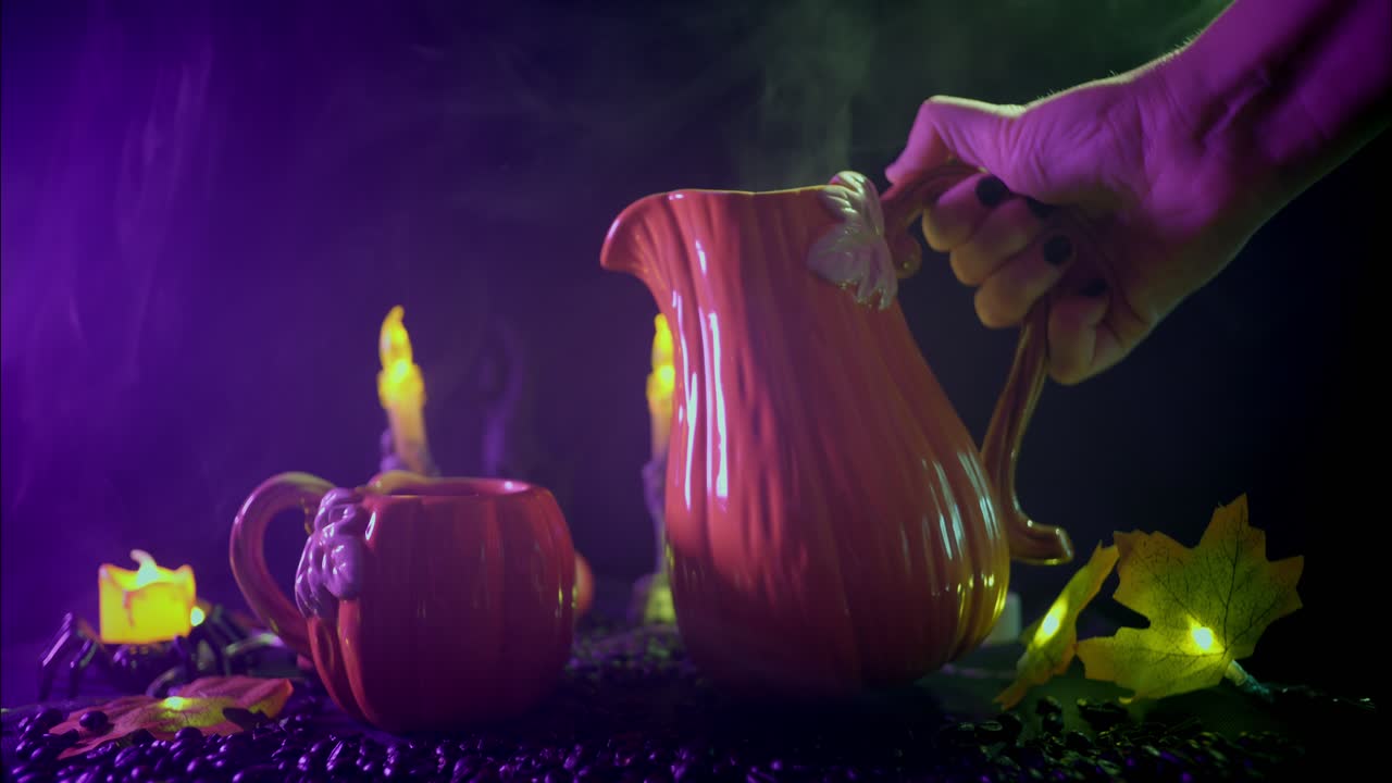 Käsi kaataa kuumaa juomaa kurpitsakannusta mukiin Halloween-pöydällä.