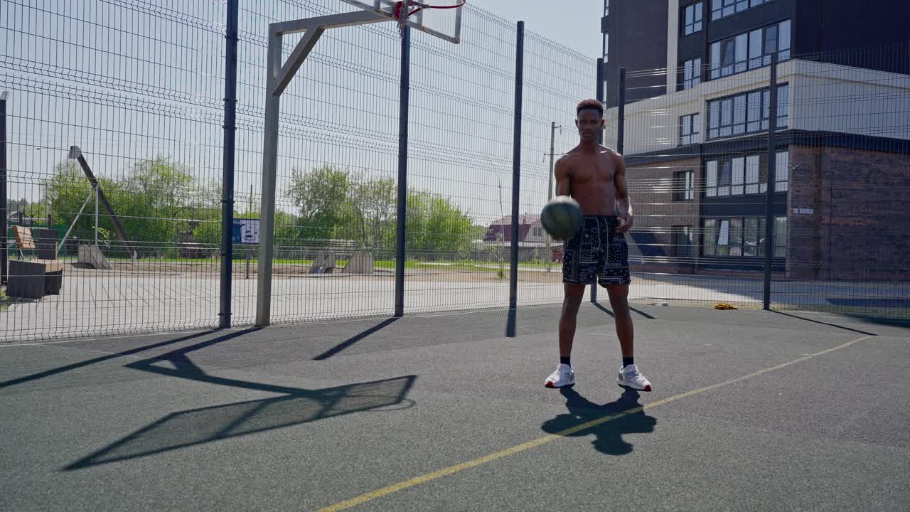 Giovane uomo afroamericano che fa roteare una palla da basket sul dito su un campo all'aperto