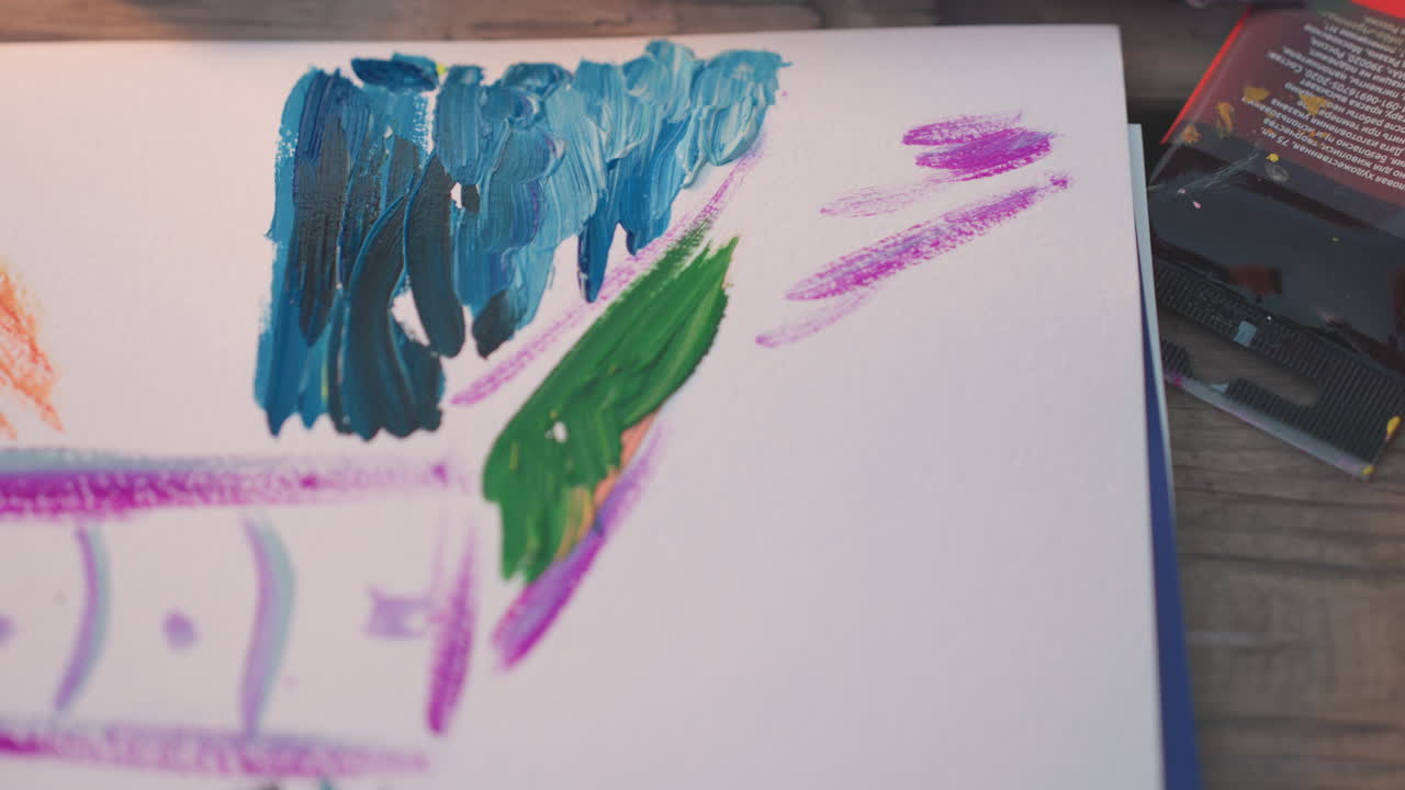 high angle artist hand holding paint brush painting tower sketch with varied colors and textured background strokes across paper during outdoor watercolor session capturing creative process