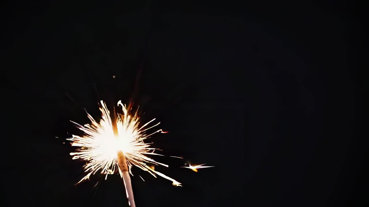 Close-up video of a sparkler against a dark background, capturing bright, dynamic sparks from a low