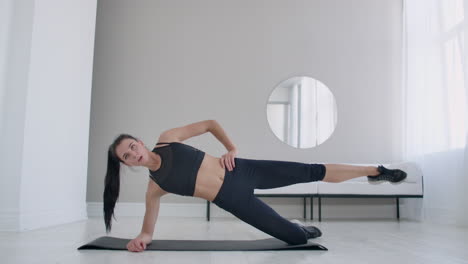 the brunette in the apartment does an exercise lateral plank standing on her knee and raising her leg up. fitness marathon.