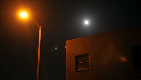 time lapse of moon rising over a house and street lamp